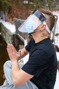 Side view of man with hands clasped wearing mask sitting outdoors