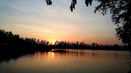 Silhouette trees by lake against sky during sunset