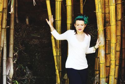 Portrait of young woman standing on tree trunk