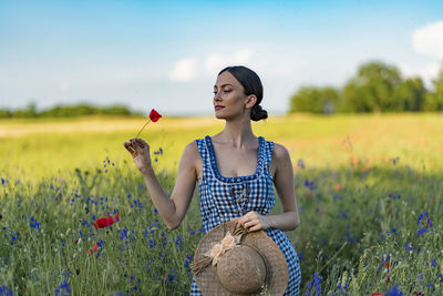Young woman standing on field against sky