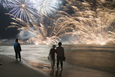People at beach against firework display during night