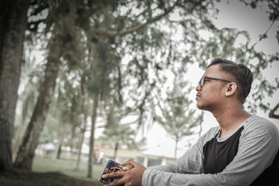 Side view of young man with phone sitting in park