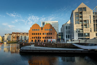 Buildings by river against sky in city