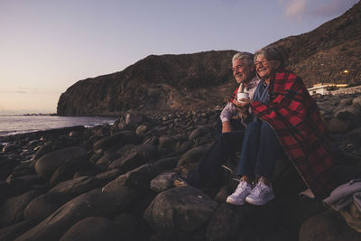 Couple sitting on rocks against sky at beach