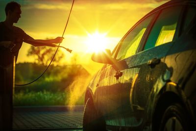 Silhouette worker washing car against sky during sunset