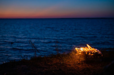 Bonfire by sea against sky at sunset