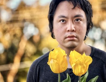 Close-up portrait of young man with yellow tulips against trees at sunset.