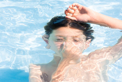 Shirtless boy holding nose while swimming in pool