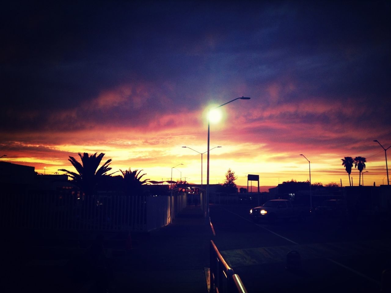 sunset, sky, transportation, silhouette, car, palm tree, orange color, cloud - sky, land vehicle, road, street light, mode of transport, tree, beauty in nature, dramatic sky, street, cloud, scenics, nature, cloudy