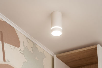 Low angle view of illuminated light bulb against wall at home