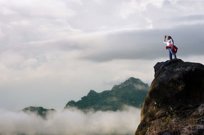 Low angle view of woman standing on cliff against sky