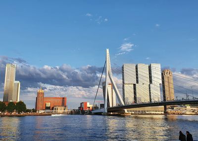 Bridge over river by city buildings against sky