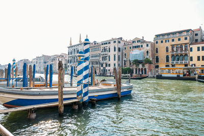 Boats moored in canal by buildings against sky