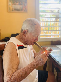 Man sitting on table at home lighting a cuban cigar.