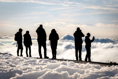 Silhouette people standing amidst fog covered mountain peak against sky