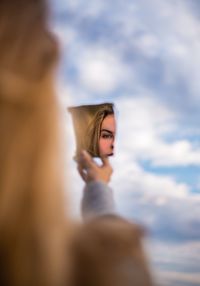Teenage girl reflecting on mirror against cloudy sky