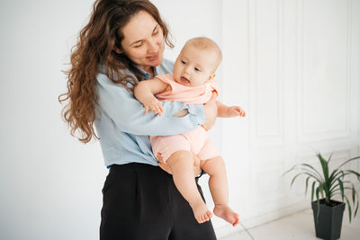 Young mother with long hair and in a shirt holds a newborn daughter. in the arms of a 6 month old 