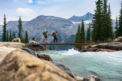 Hikers crossing glacial river over twin falls along the whaleback