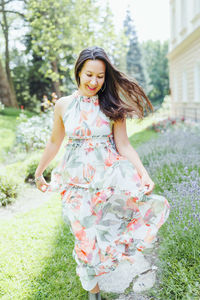 Happy multiracial japanese woman in romantic floral maxi dress in summer park