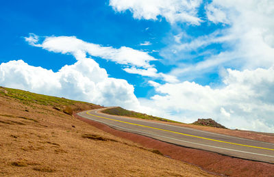 Empty road by field against blue sky