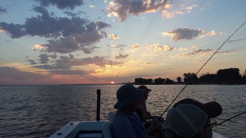 Rear view of man fishing in sea against sunset sky