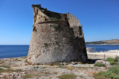 Stone wall by sea against clear blue sky