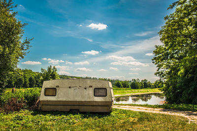 Vehicle on field by lake against cloudy sky during sunny day