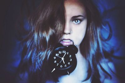 Close-up portrait of young woman carrying alarm clock in mouth