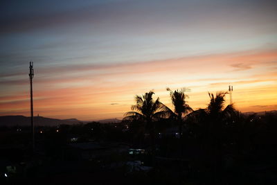 Silhouette trees on landscape against orange sky