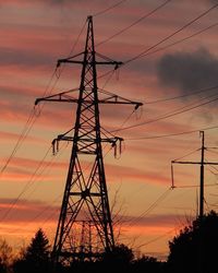 Low angle view of electricity pylon against sky at sunset