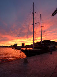 Silhouette sailboats on sea against orange sky