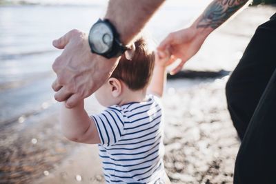 Midsection of father helping son to walk at beach