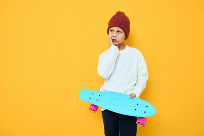 Portrait of young woman standing against yellow background