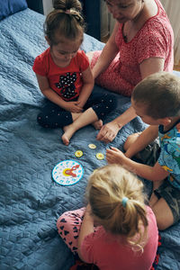 High angle view of people sitting by toy clock on bed