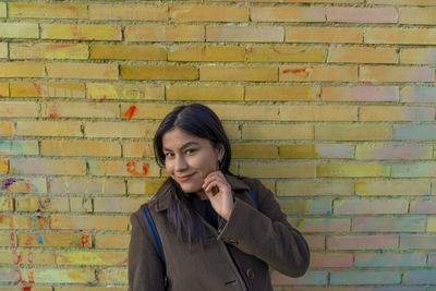 Portrait of young woman standing against brick wall