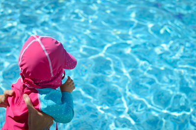 Cropped image of hands holding baby over swimming pool