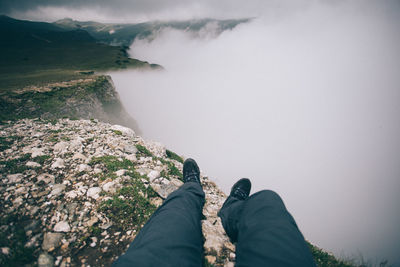 Low section of man lying on mountain peak against fog