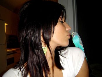 Woman kissing bird at home