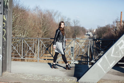 Portrait of beautiful young woman walking on footbridge during sunny day