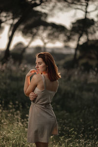 Young woman looking away while standing on field