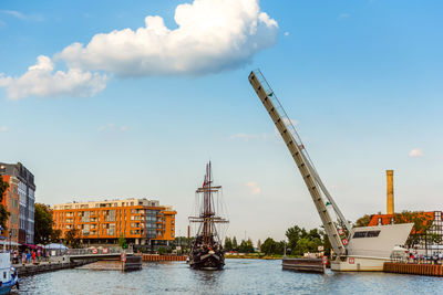 Cranes by river against sky in city