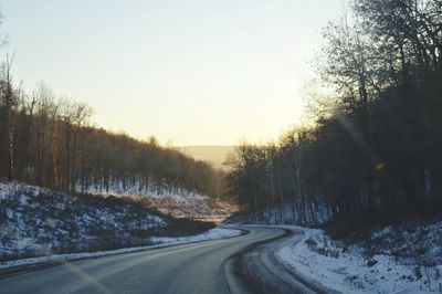 Road amidst trees against clear sky during winter