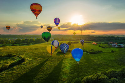 Hot air balloons flying over field against sky during sunset