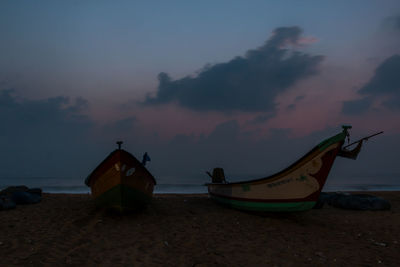 Abandoned boat on beach against sky during sunset