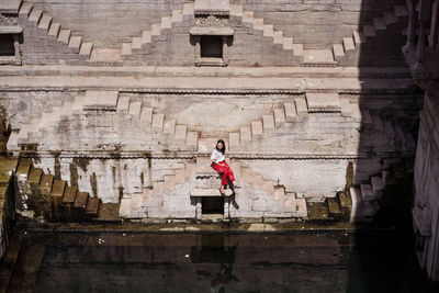 From above young ethnic female tourist sitting on steps of toorji well with water during sightseeing in india