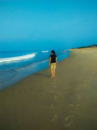 Rear view of young woman standing at beach against clear blue sky