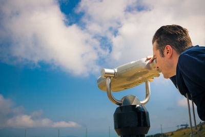 Man looking through coin-operated binoculars against sky