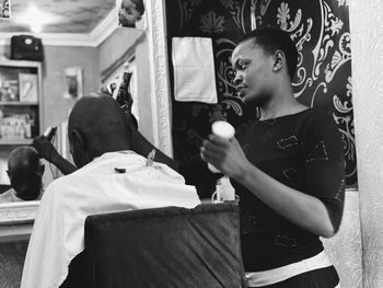 Hairdresser shaving customer head in salon