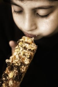 Close-up of boy eating dessert over black background