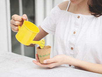 Caucasian teenage girl in a white shirt holds a yellow watering can with her hands